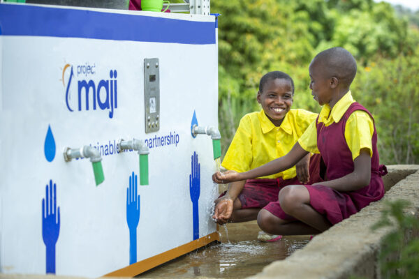 Two African children smiling while getting water from a kiosk