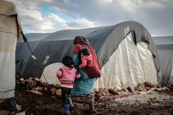 A mother walks with her young children at a Syrian refugee camp