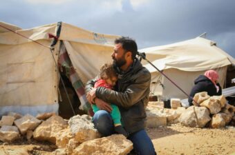man holding his daughter at a campsite for displaced families