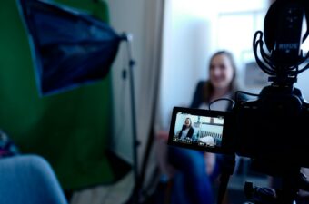 Photo of a video camera setup for an interview, with a blurry woman behind the camera.