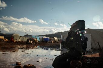 Syrian girl blowing bubbles in refugee camp.